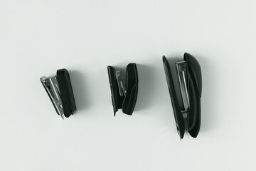 Three black office staplers for paper of different sizes. White background.