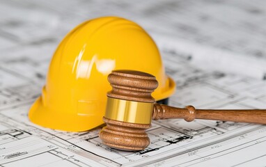 A yellow hard hat and a wooden gavel rest on architectural blueprints, symbolizing construction law and safety in the building industry.