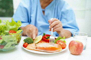 Asian elderly woman patient eating salmon stake and vegetable salad for healthy food in hospital.