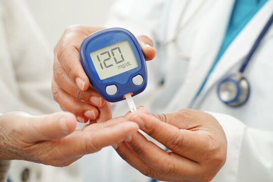 Asian doctor using digital glucose meter for check sample blood sugar level to treatment diabetes.