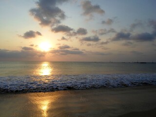 Fototapeta premium Serene Sunset on a Beach with a Cloudy Sky and Waves Lapping at the Shoreline