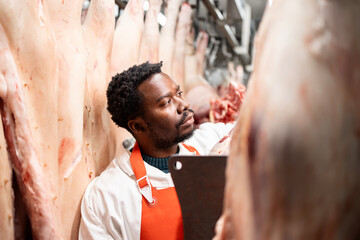 Man butcher working in food factory, cutting raw meat for processing.