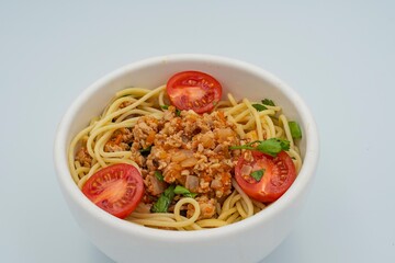 Delicious pasta bolognese with meat sauce, cherry tomatoes and parsley in a bowl on a white background. Italian cuisine dish.