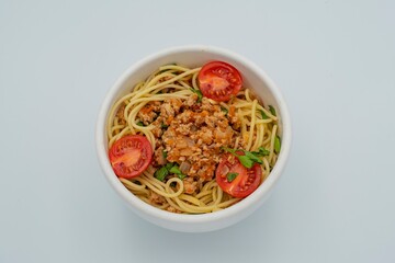 Delicious pasta bolognese with meat sauce, cherry tomatoes and parsley in a bowl on a white background. Italian cuisine dish.