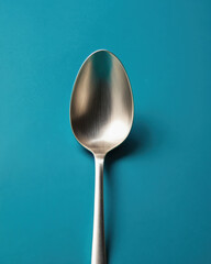 A simple, elegant stainless steel spoon resting on a vibrant turquoise background, perfect for culinary and kitchen themes.