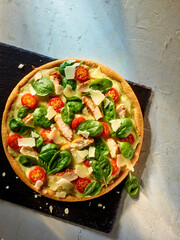 Pizza mit Haehnchen und Spinat mit Tomatenstuecken auf Schiefer und grauem rustikalem Fond, Pizza,...