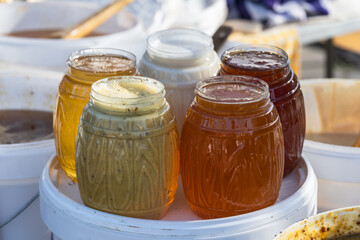 Plastic jars with different types of honey on a market stall, honey trade. Selective focus.