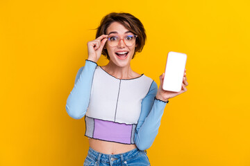 Photo of astonished charming lady touch eyeglasses demonstrate empty space smart phone screen...