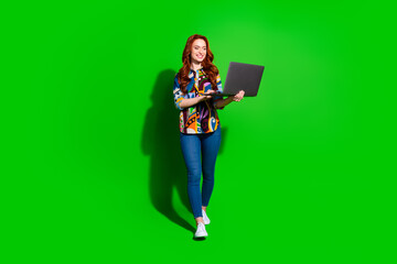 Stylish young woman with red hair holding a laptop on a vibrant green background