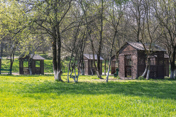 Obraz premium Wooden gazebos for relaxing in the park. A place for a family vacation in nature. A place for cooking shish kebab. Outdoor recreation in spring. Flowering trees.