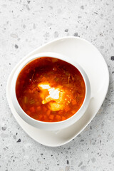 A bowl of rich red soup served with a dollop of cream, showcasing vibrant vegetables in a smooth broth on a textured surface