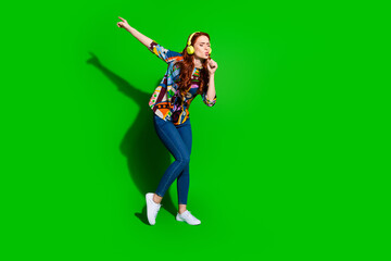 Joyful young woman singing and posing with headphones on a green background
