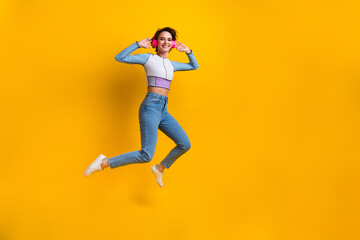 Full length photo of carefree nice person jump arms touch headphones empty space isolated on yellow color background