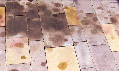 Stained paving tiles with dark and rusty spots, possibly caused by oil, rust, or water damage....