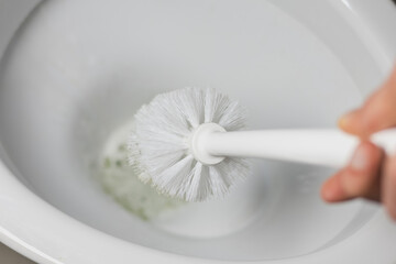 White toilet brush in people hand. Cleaning toilet bowl concept. Close up.