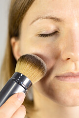 Vertical photo of Application of mattifying powder for face.The girl is sweeping the brush back and...