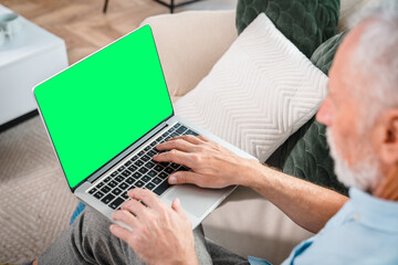 Handsome senior old man using a laptop with mock up blank screen while sitting relaxing resting on...