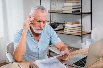 Serious mature man wearing glasses sitting on table home office manage budget received invoice...