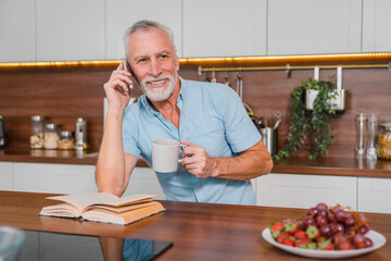 Elderly man in kitchen talking on the phone in his home. Happy, communication and 5g network with senior male enjoying fast internet and online app conversation.