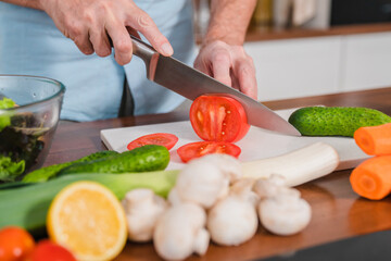 Close Up Shot of a Man Chopping a Tomato with a Sharp Kitchen Knife. Preparing a Healthy Organic Salad Meal in a Modern Kitchen. Natural Clean Diet and Healthy Way of Life Concept.