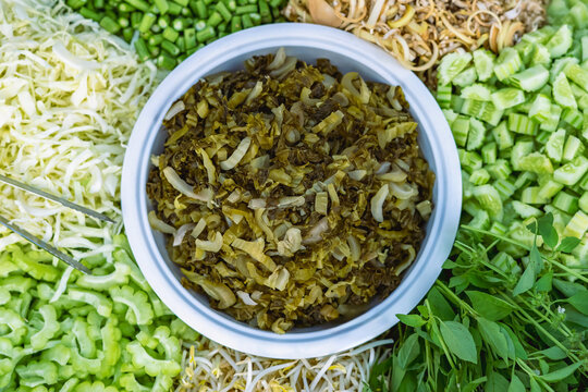 Chopped sour pickled green mustard in white bowl with Various side dishes such as pickled vegetable, fresh salad and fruit for eat with main course of rice vermicelli, rice and curry of Thai food.