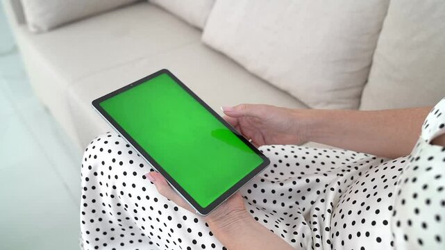 Woman Holding Tablet with Green Screen Sitting on Sofa, Using Touch screen, Browsing Digital Content, Engaging with Mobile Technology, Cozy Bright Living Room, Modern Communication.