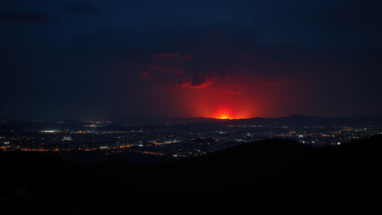 Nighttime view of a city with a wildfire burning in the distance.