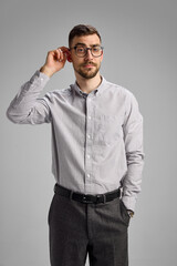 Portrait of thoughtful businessman in formal wear and glasses, standing with contemplation against grey studio background. Concept of business, lifestyle, emotions