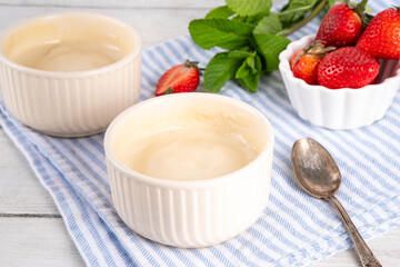 Vanilla or white chocolate pudding dessert, in ceramic portioned bowl on kitchen table, with fresh strawberries