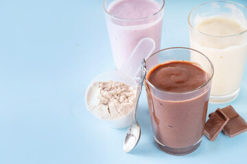 Quick and simple protein pudding. Healthy summer cold dessert. Three glasses with vanilla, chocolate and berry protein pudding, with chocolate slices, fresh strawberry, blueberry, protein powder scoop