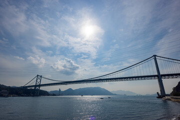青空と太陽光に照らされる関門橋と光る海面の風景