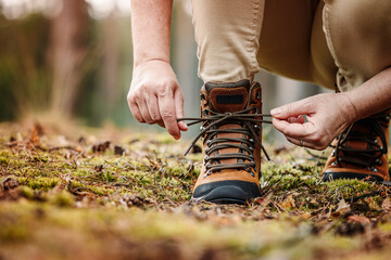 Woman tying shoelace on her hiking boot. Tourist is getting ready for hike on trekking trail in...
