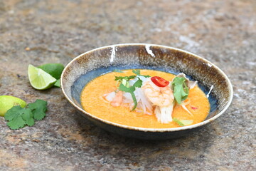 A flavorful and spicy Thai Tom Yum Goong soup with shrimp, rice noodles, and a rich coconut milk broth. Garnished with fresh cilantro and red chili, 