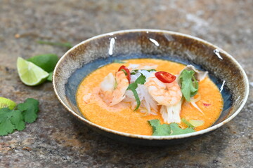 A flavorful and spicy Thai Tom Yum Goong soup with shrimp, rice noodles, and a rich coconut milk broth. Garnished with fresh cilantro and red chili, 