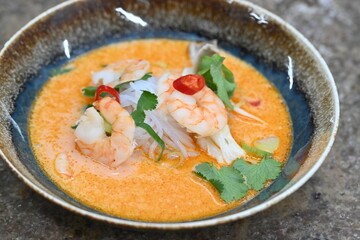 A flavorful and spicy Thai Tom Yum Goong soup with shrimp, rice noodles, and a rich coconut milk broth. Garnished with fresh cilantro and red chili, 