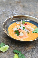 A flavorful and spicy Thai Tom Yum Goong soup with shrimp, rice noodles, and a rich coconut milk broth. Garnished with fresh cilantro and red chili, 