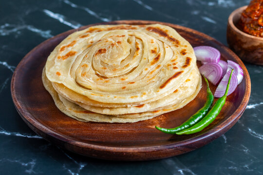 Crispy, flaky laccha paratha served hot with tangy pickle, fresh onion slices, and spicy green chili for a perfect flavor burst.
