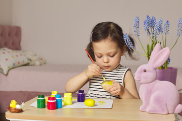Little child girl paint Easter eggs at home. kid is preparing for Easter.