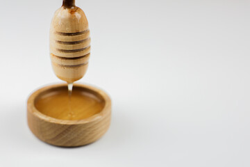 Close-up of honey dripping from a wooden honey spoon that stands vertically over a wooden bowl on a...