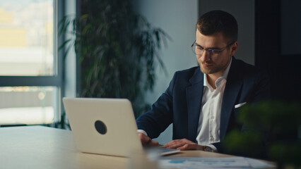 Young businessman, executive, accountant or project manager in a suit working on a laptop at a...