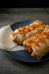  an artisan chicken bake with exposed ground beef and cheese filling, presented on a black plate with a dark background in a dark food style. The soft light highlights the golden crust texture 