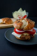  A juicy beef burger with cucumber, tomato, and lettuce, styled in dark food aesthetics on a black plate. Captured in a vertical format for a striking visual.