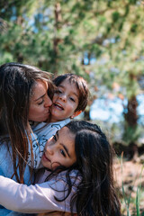 Fototapeta premium A woman is hugging two children, one of whom is wearing a shirt with a cat on it. The children are smiling and seem to be enjoying the moment. The woman is likely a mother or a close family member