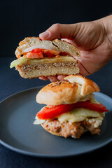  A juicy beef burger with cucumber, tomato, and lettuce, styled in dark food aesthetics on a black plate. Captured in a vertical format for a striking visual.