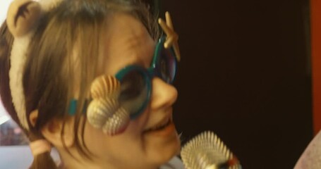 Woman wearing whimsical seashell adorned sunglasses belting out song passionately during lively karaoke event, radiating exuberant musical energy