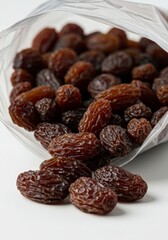 Fototapeta premium Raisins Spilling From a Plastic Bag on White Surface Close Up