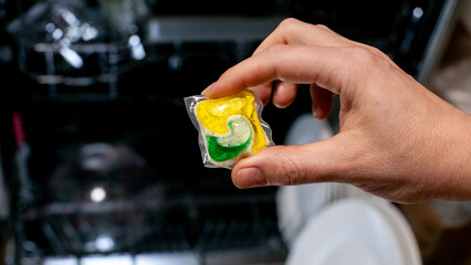 Hand holding a dishwasher detergent pod, kitchen cleaning essentials, practical household chores concept