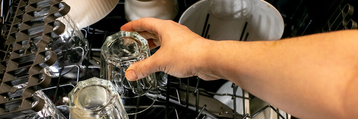 A person's hand loading clear glasses into a dishwasher, sustainability, domestic chores efficiency, cleanliness, home kitchen appliance organization