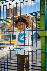 Child holding metal mesh fence smiling at playground