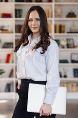 Professional young businesswoman holding a laptop in a modern office space